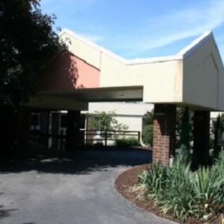 A building entrance with a driveway and surrounding trees.