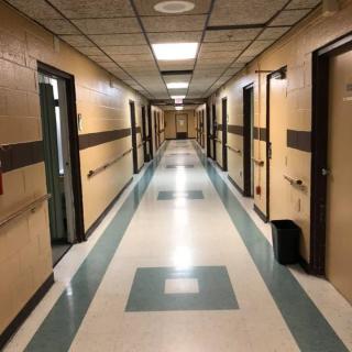 A long, empty hallway with doors along each side and fluorescent lights overhead.