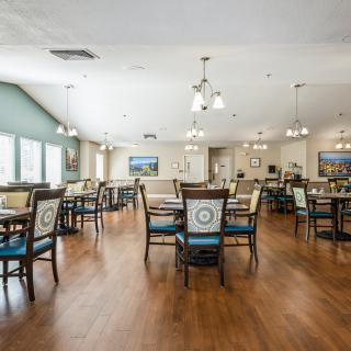A spacious and well-lit dining room with tables and chairs arranged neatly on a wooden floor.