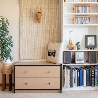 A cozy interior space featuring a bookshelf, drawer storage, and decorative elements including a plant and various books.