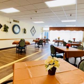 An empty dining hall with arranged tables and chairs, adorned with wall decorations and potted plants.