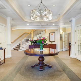 Elegant lobby with a central table adorned with flowers and a grand chandelier overhead.