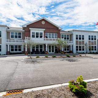 A large building with a symmetrical facade and a spacious parking area in front under a partly cloudy sky.