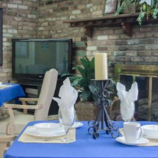 A cozy dining area with blue tablecloths and elegant place settings, set against a brick wall with a fireplace and television in the background.