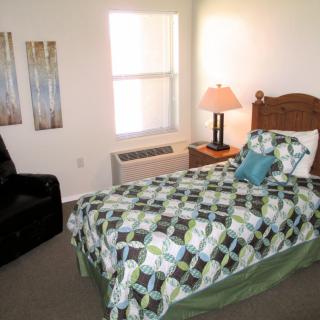 A cozy bedroom with a single bed, decorative bedding, and a bedside lamp.