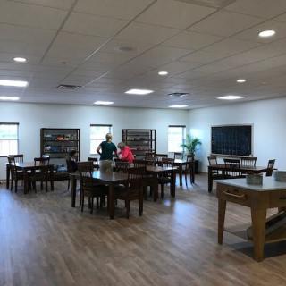 A spacious library interior with tables and bookshelves, where people are engaged in activities.