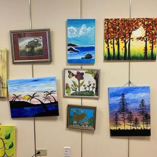A collection of colorful paintings displayed on a gallery wall, featuring various landscapes and nature scenes.