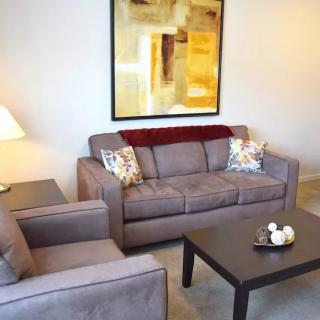 A cozy living room with a sofa, armchair, and coffee table, complemented by a lamp and wall artwork.