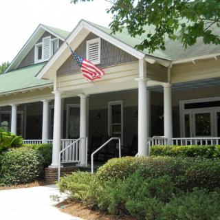 A charming house with an American flag, featuring a porch with columns and surrounded by lush landscaping.