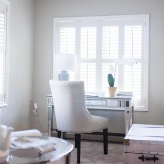 A minimalist home office setup with a white chair and desk near a large window.
