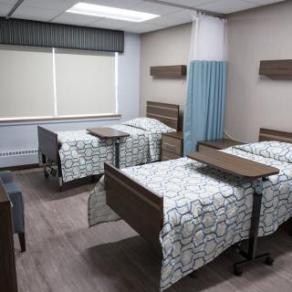 A hospital room featuring two beds with medical bed tables and curtains for privacy.