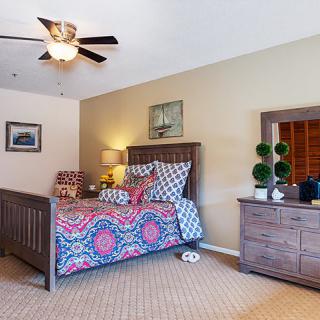 A cozy bedroom featuring a wooden bed with colorful bedding, a matching dresser, and decorative artwork on the walls.