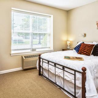A cozy bedroom with a white bed, natural light streaming through the window, and minimal decor.