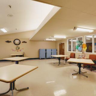 A spacious community room featuring tables and chairs, complemented by natural lighting from large windows.
