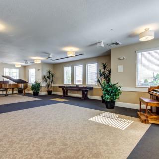 A spacious game room featuring a pool table and piano, with ample natural light from large windows and decorated with potted plants.