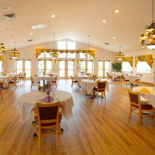 A spacious and well-lit dining room with wooden floors, neatly arranged tables, and comfortable chairs.