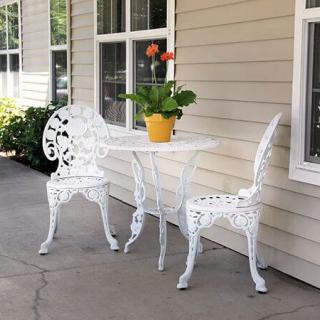 A charming patio setup with white cast iron chairs, a matching table, and a potted plant with red flowers.