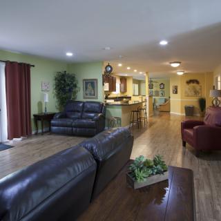 A spacious open-plan living area with a view of the kitchen, featuring leather sofas and warm wooden flooring.
