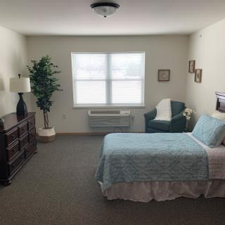 A cozy, well-lit bedroom featuring a single bed, a comfortable chair, and decorative touches.
