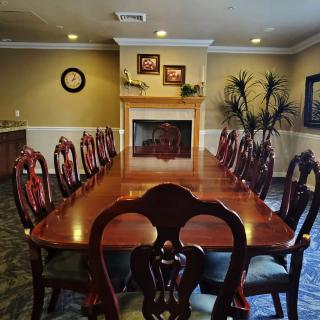 A classic dining room featuring a long wooden table surrounded by elegant chairs, with a fireplace and decorative elements in the background.