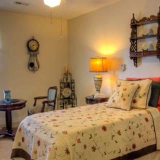 A cozy vintage-style bedroom with a single bed, decorated with floral bedding and complemented by antique furnishings.