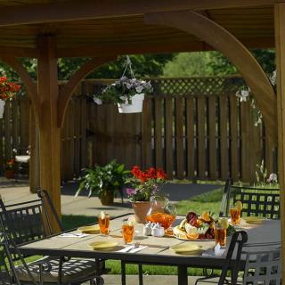 An inviting outdoor dining area under a pergola, featuring a table set with drinks and snacks, surrounded by lush garden plants.