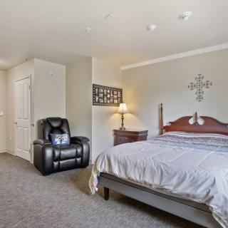 A cozy bedroom featuring a large bed, armchair, side table with a lamp, and decorative wall elements.