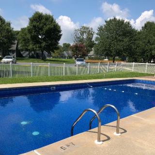 A sunny day view of an outdoor swimming pool surrounded by a fence and greenery.