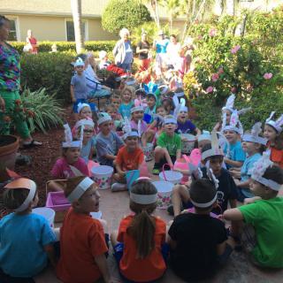A group of children gathered outdoors, wearing colorful hats in a garden setting.