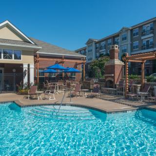 A sunny day at a residential apartment complex featuring an outdoor swimming pool and patio area.