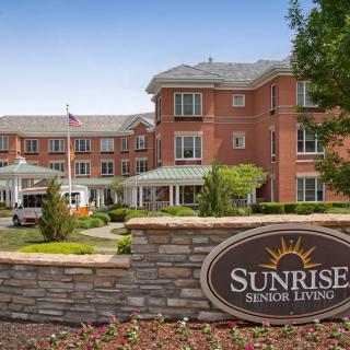 A senior living facility with a brick exterior and well-maintained landscaping, featuring a prominent sign labeled 'Sunrise Senior Living'.