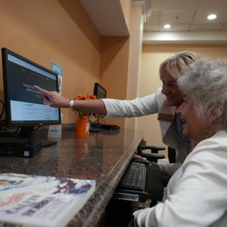 An elderly person receives guidance on using a computer.