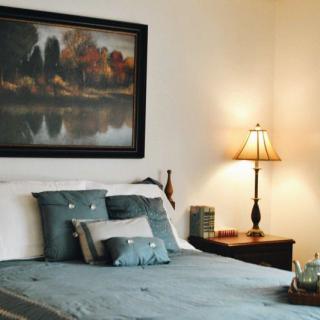 A cozy bedroom with a neatly made bed, decorative pillows, and a bedside lamp.