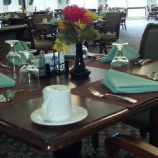A neatly set dining table in a restaurant with a flower arrangement, glasses, napkins, and a cup.