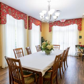 A well-lit dining room featuring a large table with multiple chairs, adorned with floral decorations and illuminated by a chandelier.