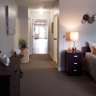 A cozy bedroom with a hallway view, featuring a bedside table and lamp.
