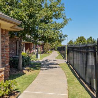 A scenic view of a pathway lined with trees and residential buildings, bordered by a black fence on one side.