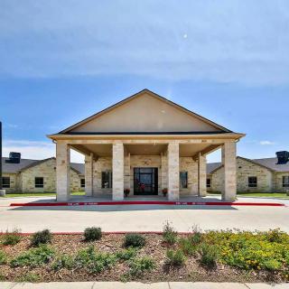 A symmetrical building entrance with stone columns and landscaped surroundings under a clear sky.