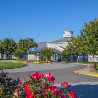 A scenic view of a building surrounded by gardens with vibrant flowers and lush trees under a clear blue sky.