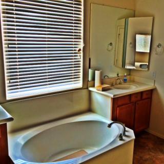 A cozy bathroom featuring a bathtub, sink, and mirror with natural light coming through the window blinds.