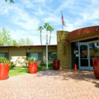 A modern building entrance with large red planters, an American flag, and palm trees under a clear blue sky.