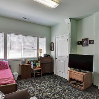A cozy room featuring a bed, television, and various furnishings under natural light through large windows.
