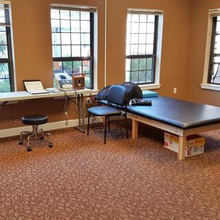 A therapy room featuring a treatment table and exercise equipment near large windows.