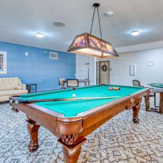 A spacious game room featuring a pool table under stylish lighting, with comfortable seating in the background.