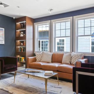 A modern living room with a leather sofa, coffee table, and built-in bookshelf by the windows.