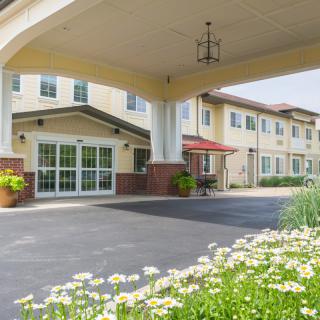Entrance to a two-story building with a covered driveway and landscaped surroundings.