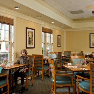 A cozy dining area with wooden tables and chairs, featuring wall art and natural light from large windows.