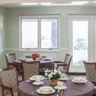 A well-lit dining room with several round tables set for a meal, featuring elegant tableware and floral centerpieces.