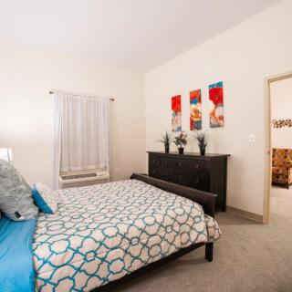A modern bedroom with minimalist decor, featuring a comfortable bed, bedside table, dresser, and vibrant artwork on the wall.