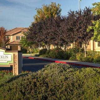 Entrance of an apartment complex with lush landscaping and clear signage.